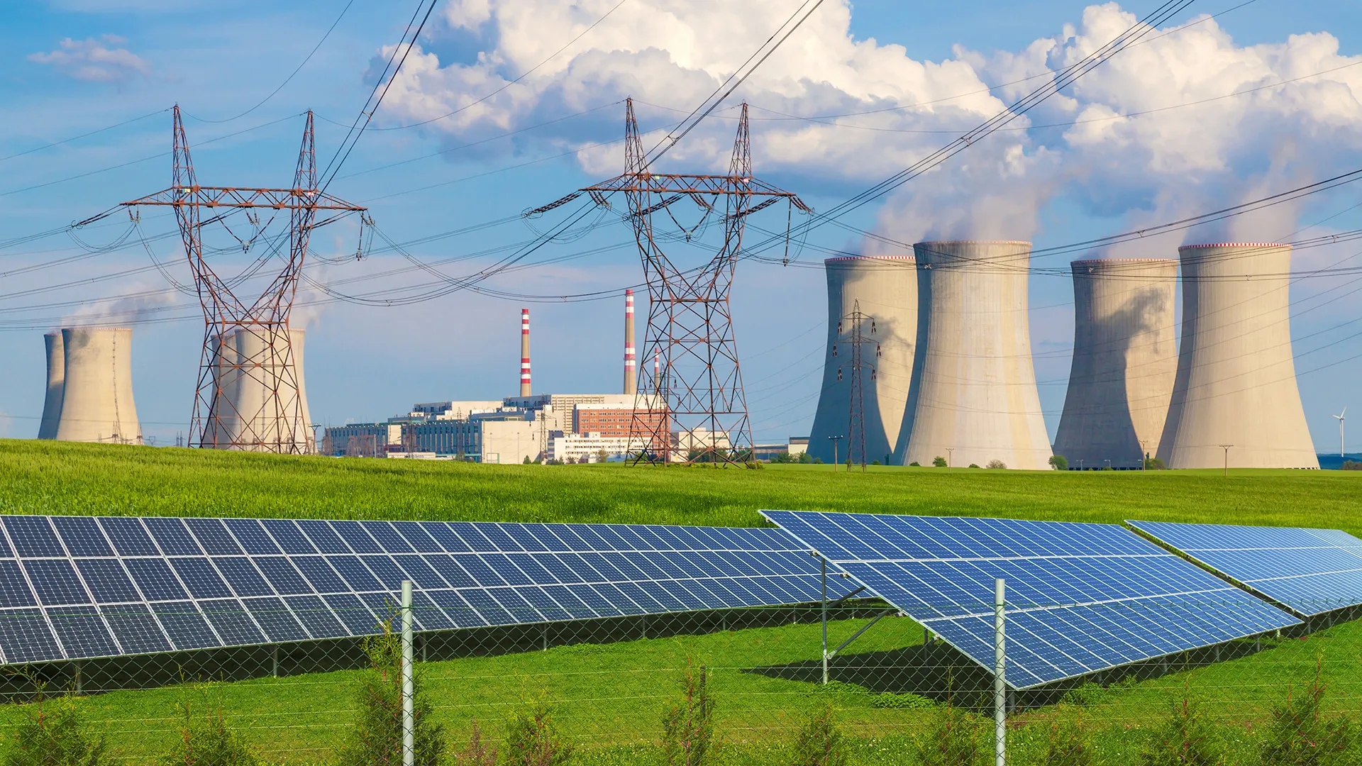 Solar panels in a field with a power station in the horizon. 