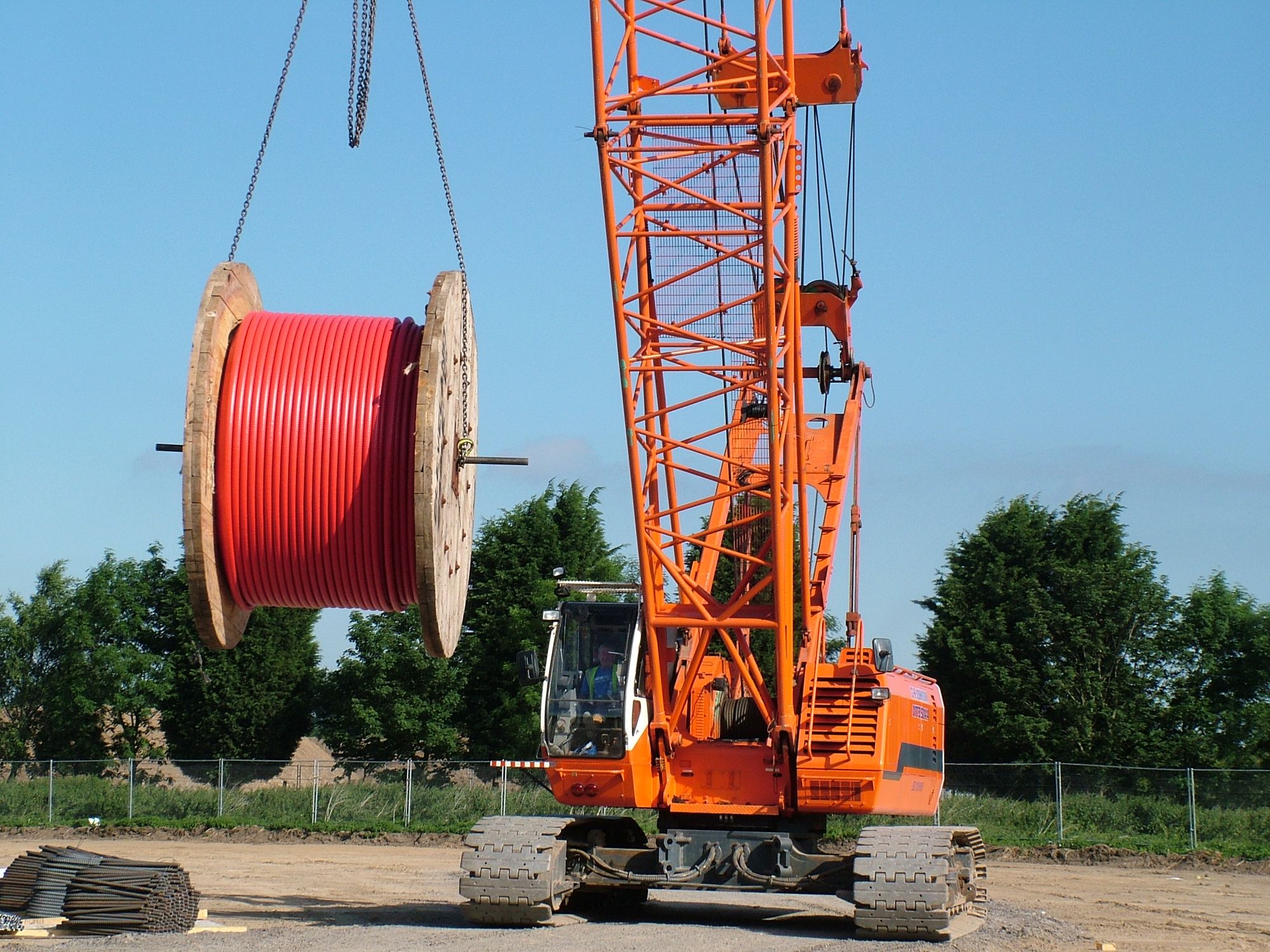 A high voltage cable spool held up by a crane that will require electricians to solve various challenges in order for it to be properly installed. 