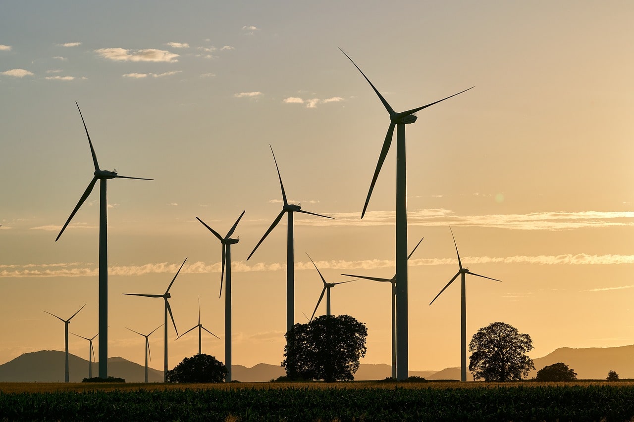 A wind farm on an expanse of grass at sunrise with trees and hills in the background